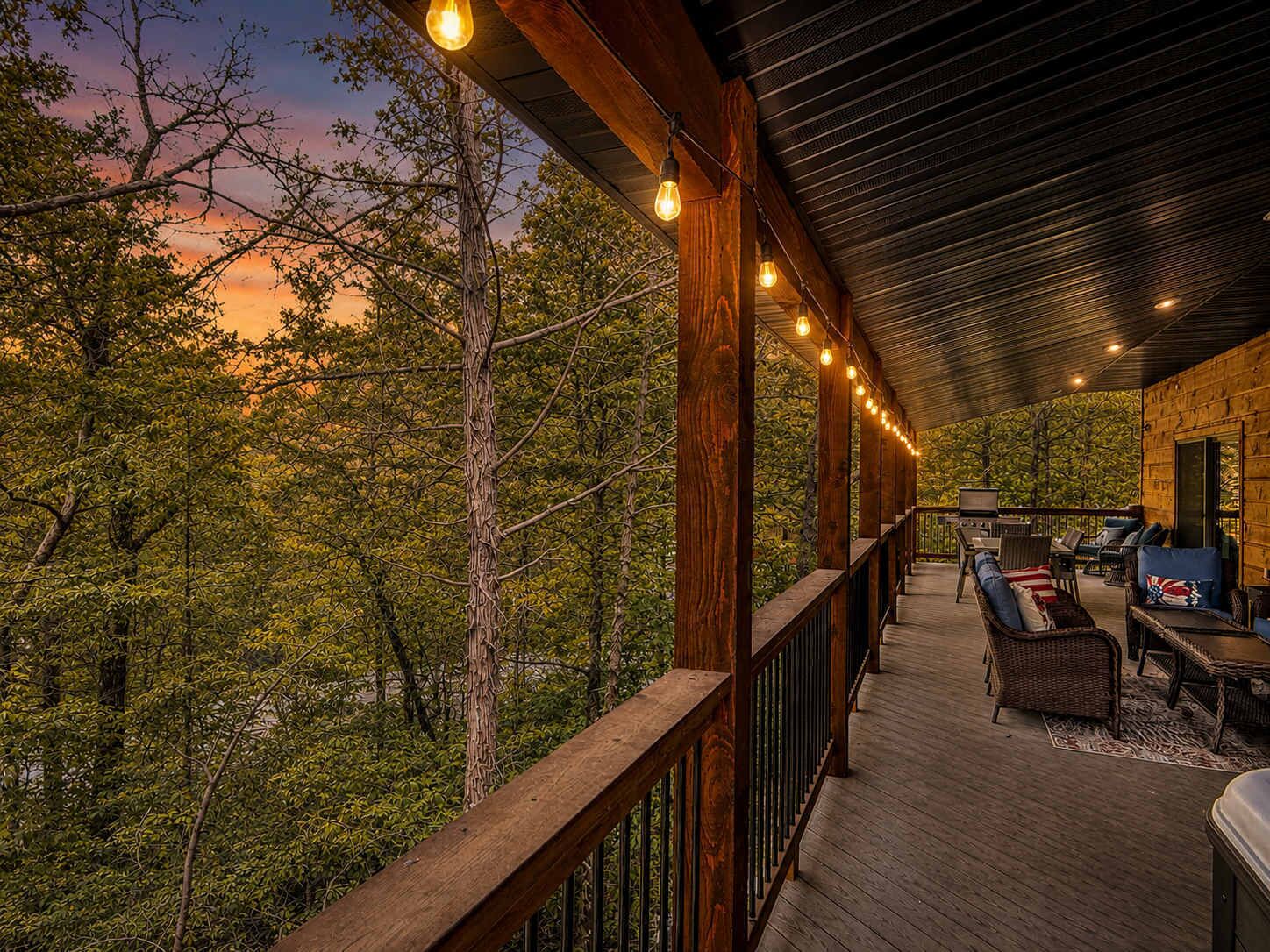 A covered outdoor deck with a wooden railing, furnished with sofas and a television.
