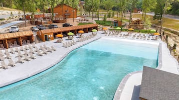 A resort with a large swimming pool, lounge chairs, and a wooden cabin structure.