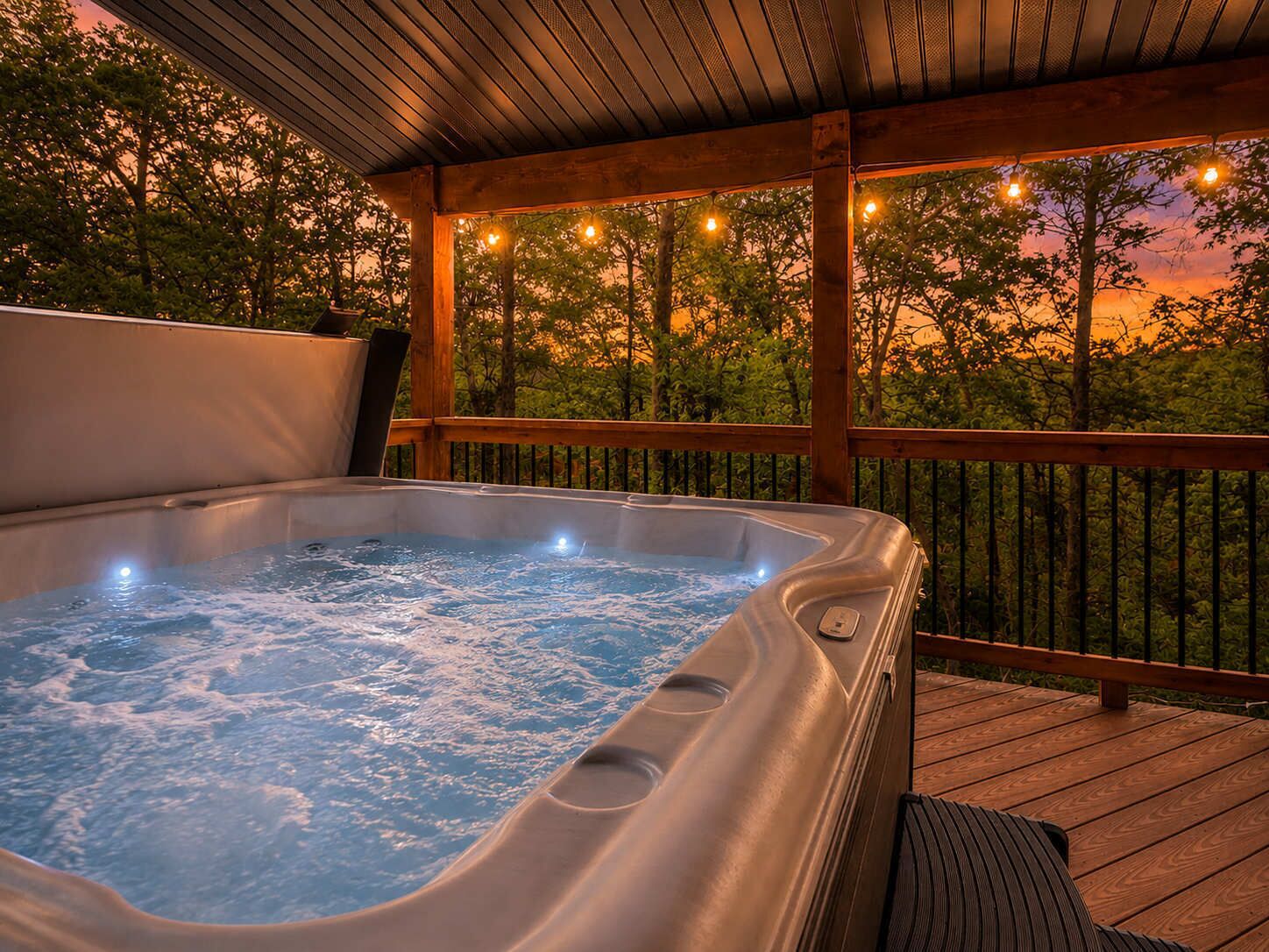 A hot tub on a wooden deck with a view of trees and a sunset.