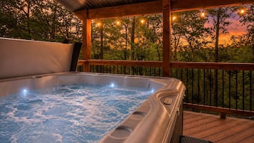 A hot tub on a wooden deck with a view of trees and a sunset.