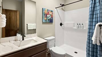 Une salle de bain avec un lavabo blanc, des toilettes, une douche avec un rideau bleu et un tableau accroché au mur.