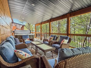 Een overdekt terras met rieten meubilair, een barbecue en uitzicht op de omliggende bomen.
