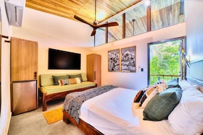 Un dormitorio con cama, sofá, televisor y ventana con vista a zonas verdes.