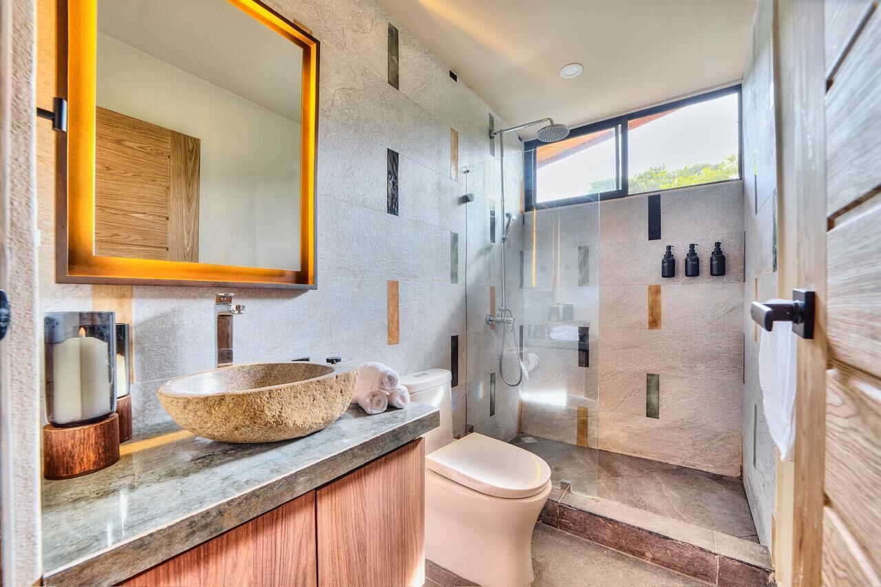 Een moderne badkamer met een grote spiegel, een stenen wastafel, een douche met glazen wanden en een toilet.