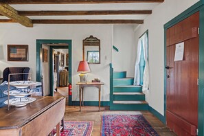 A room with a wooden staircase, a table with a lamp, and a rug. - A 1787 home older than the country it stands in (Fredericksburg)