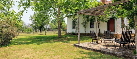 Ein weißes Gebäude mit einer Holzpergola, Sitzgelegenheiten im Freien und einem eingezäunten Hof.