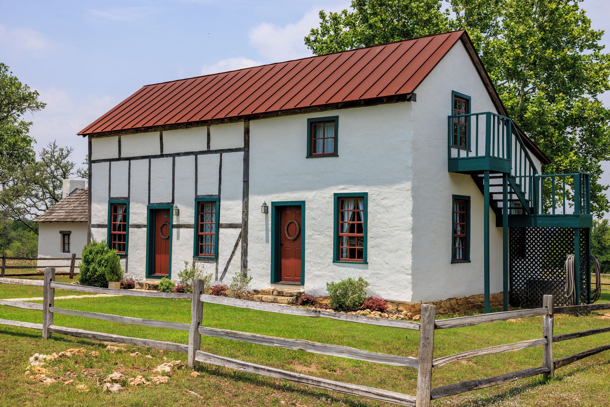 A two-story white building with a red roof, green window frames, and a wooden fence in front.