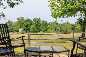 Un área de estar al aire libre con una mesa y sillas, rodeada por una valla de madera, con árboles y un molino de viento al fondo.