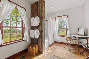 Una habitación con ventanas amplias, una puerta de madera, una silla, una mesa y un espejo.