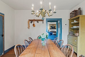 A dining room with a wooden table, chairs, a chandelier, and a blue door leading to another room. - A 1787 home older than the country it stands in (Fredericksburg)