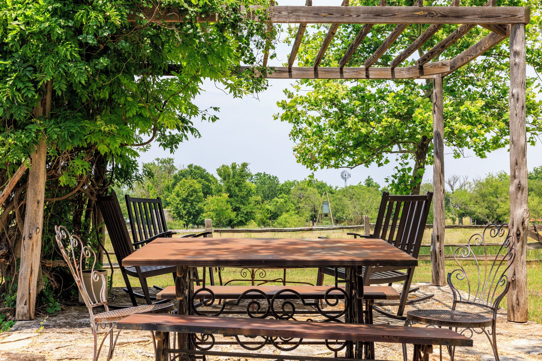 Un área de comedor al aire libre con una pérgola de madera, sillas de metal y una mesa.