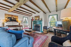 A traditional living room with exposed wooden beams, a fireplace, a television, and a sofa. - A 1787 home older than the country it stands in (Fredericksburg)