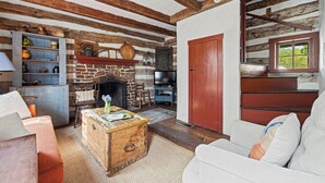 Ein rustikales Wohnzimmer mit freiliegenden Holzbalken, einem Kamin aus Stein, einem Fernseher und einer gemütlichen Sitzecke.