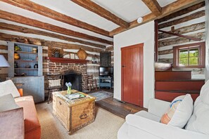 Un salon rustique avec des poutres apparentes, une cheminée en pierre, un téléviseur et un coin salon confortable.