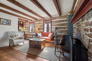 Un intérieur rustique avec des poutres apparentes, une cheminée en pierre et un coin salon confortable avec un canapé et des fauteuils.