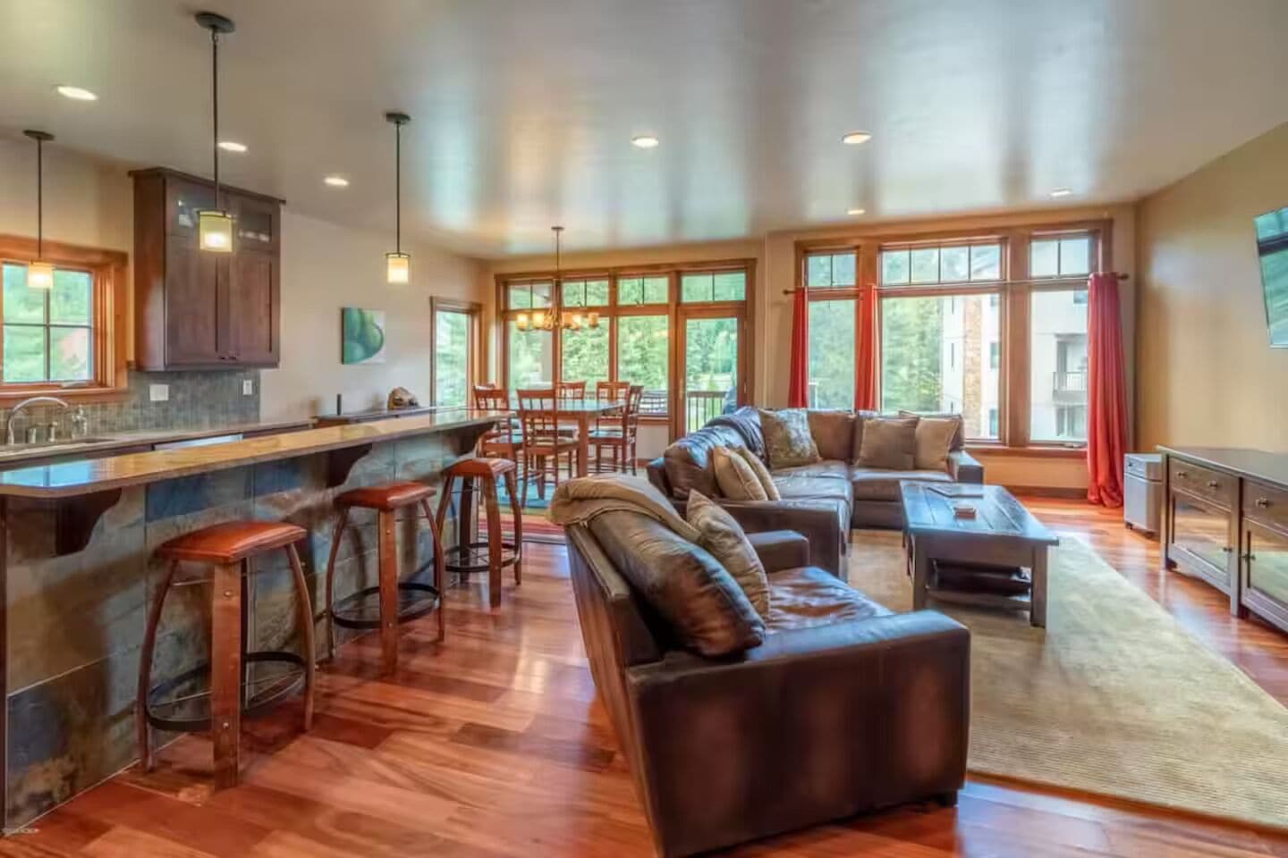 A spacious living area with a large sectional sofa, a bar area with stools, and a kitchen with wooden cabinets.