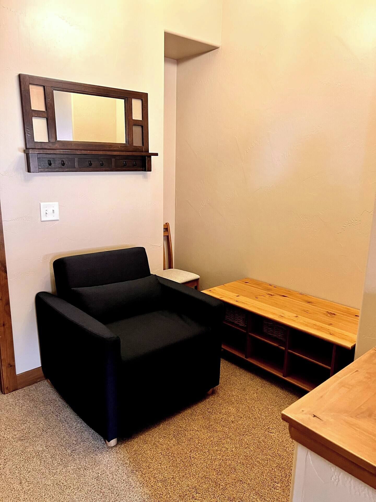 Une petite pièce avec un canapé noir, un banc en bois et un miroir fixé au mur.