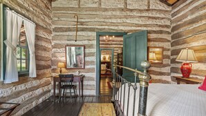 Ein rustikales Blockhauszimmer mit einem Holztisch, einem Stuhl, einem Bett mit Patchworkdecke und einer Treppe, die in einen anderen Raum führt.