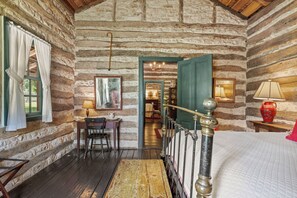 A rustic log cabin room with a wooden desk, a chair, a bed with a quilt, and a staircase leading to another room. - An 1865 cabin, home to four generations (Fredericksburg)
