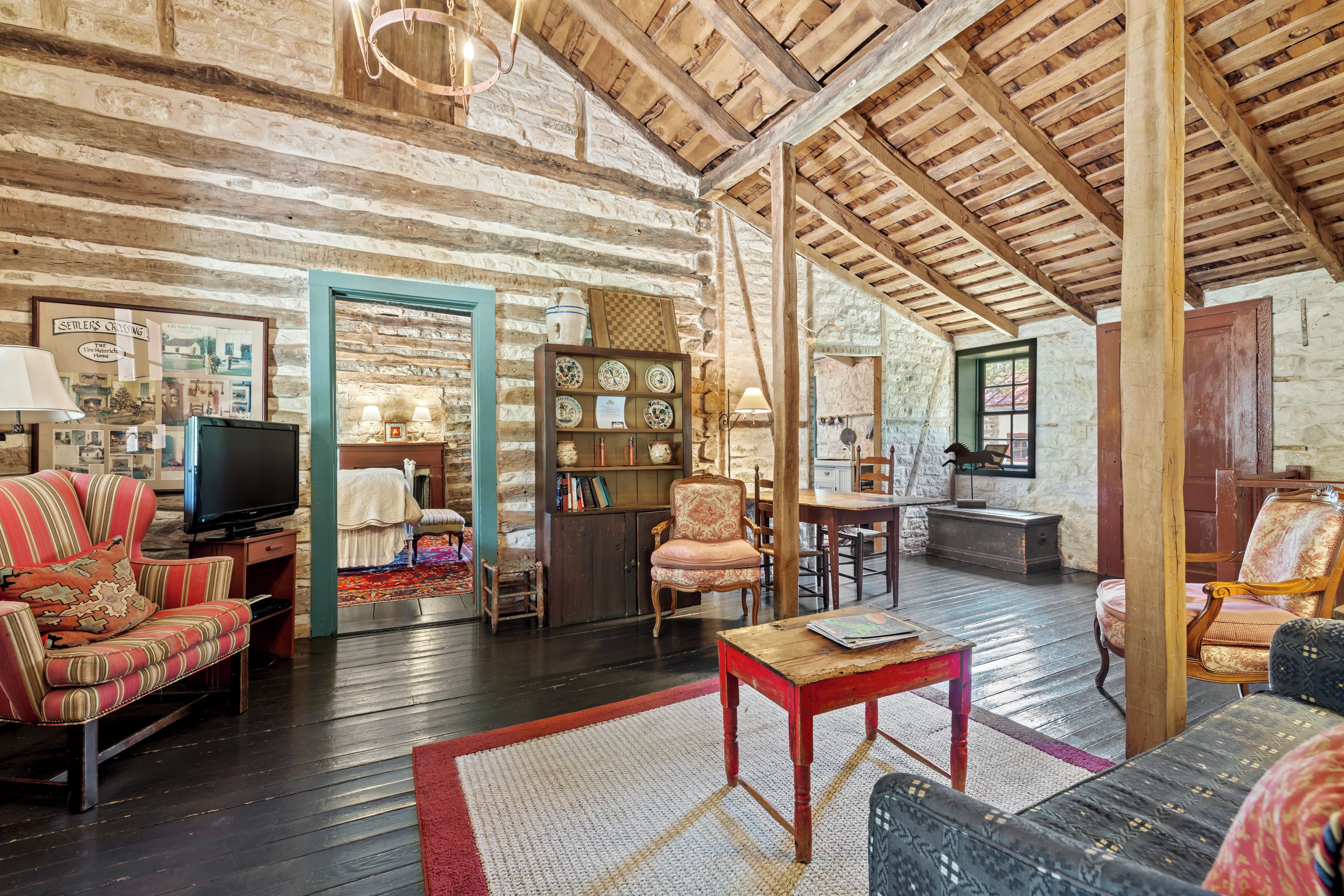A rustic interior with exposed wooden beams, a television, and a variety of seating including a striped armchair and a patterned sofa.