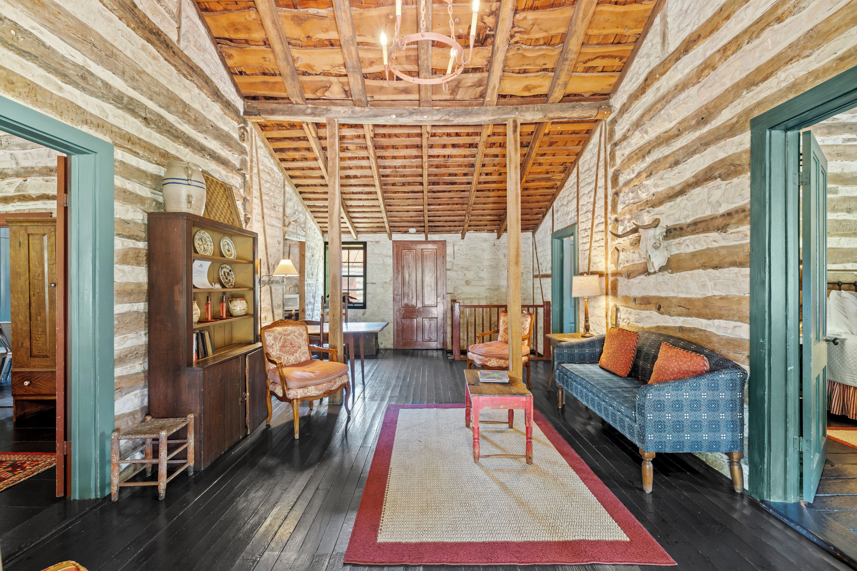 A log cabin interior with a wooden ceiling, a sofa, a dining table, and a fireplace.