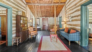 Ein Holzhaus-Interieur mit Holzbalkendecke, einer Couch, einem Esstisch und einem Kamin.