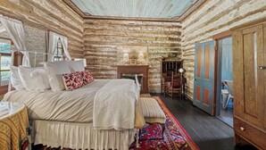 Ein Schlafzimmer in einer Blockhütte mit Bett, Nachttisch, Lampe und Blick ins Freie.