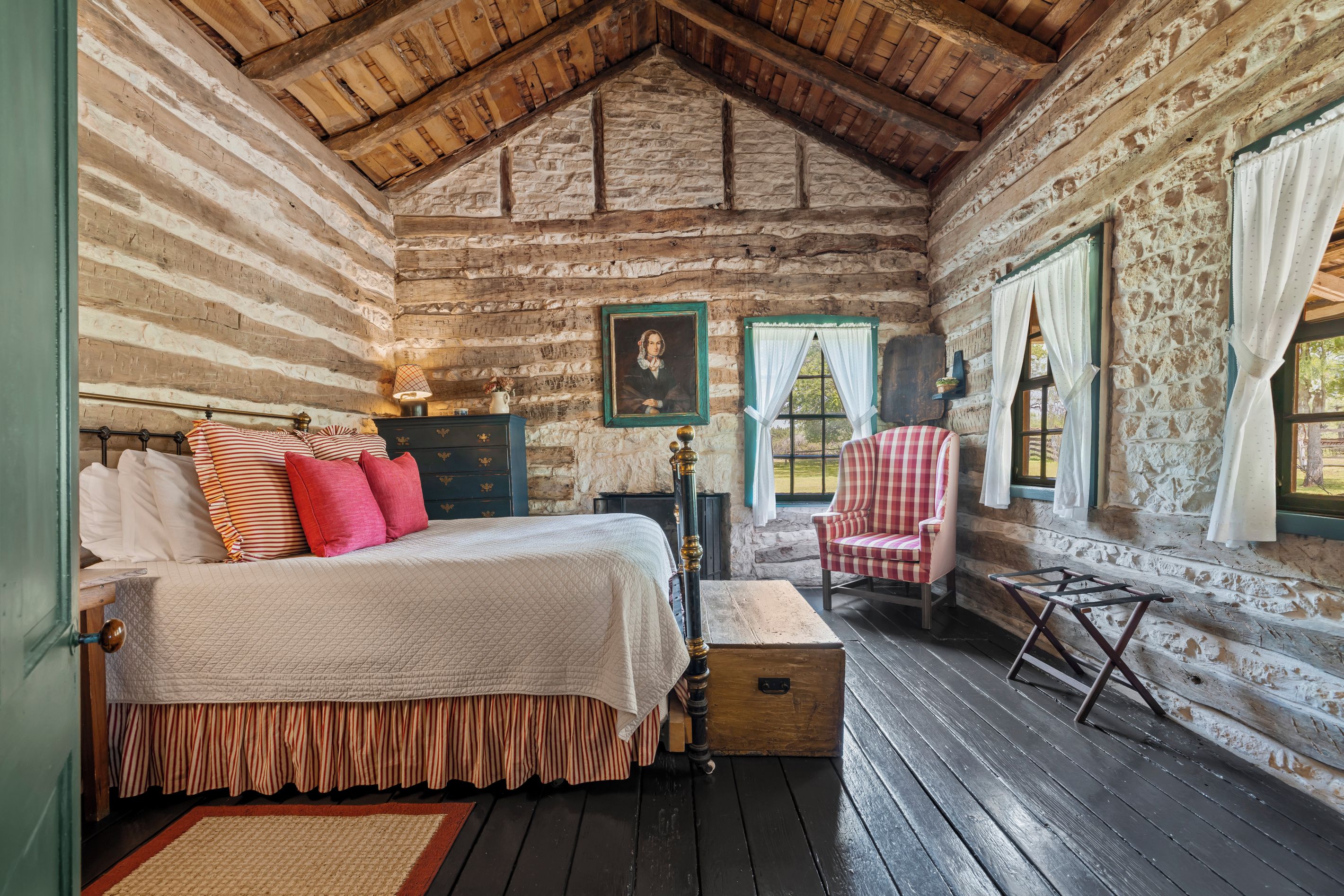 A log cabin bedroom with a bed, a chair, a dresser, and a window with curtains.