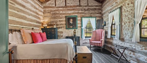 A log cabin bedroom with a bed, a chair, a dresser, and a window with curtains.