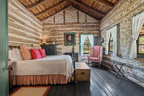 A log cabin bedroom with a bed, a chair, a dresser, and a window with curtains. - An 1865 cabin, home to four generations (Fredericksburg)