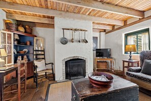 A rustic living room with a fireplace, wooden beams, a television, and a cozy seating area. - An 1865 limestone barn with gun-slot windows (Fredericksburg)