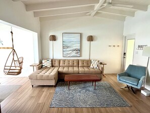 A modern living room with a sectional sofa, a blue armchair, a hanging chair, and a large abstract painting on the wall.