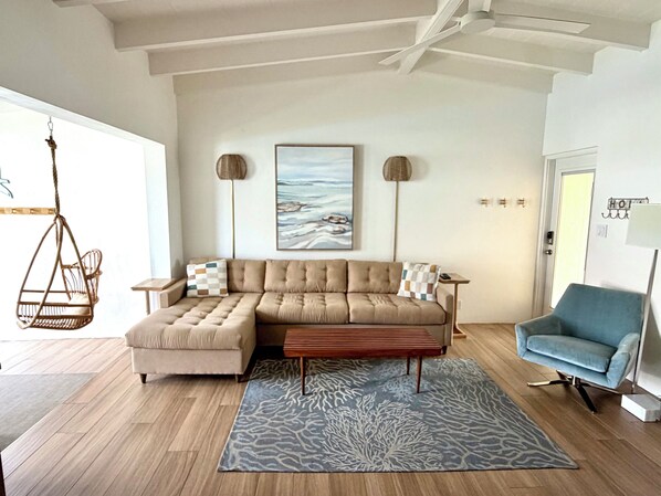 A modern living room with a sectional sofa, a blue armchair, a hanging chair, and a large abstract painting on the wall.