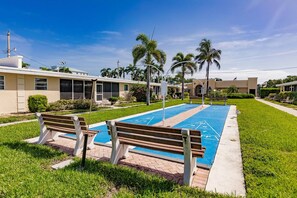 A swimming pool with a shuffleboard area, benches, and palm trees. - Siesta Key Beach Condo - Steps to Private Beach + King Bed + 2 Pools (Sarasota)