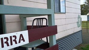 A bench with a sign reading 'IRRA' in front of a building with a window and a door.