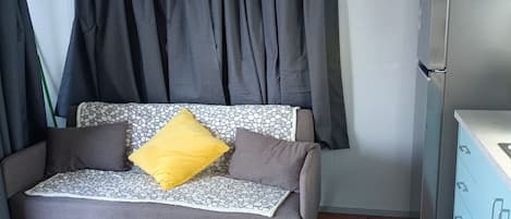 A small, single-room accommodation with a sofa bed, a refrigerator, and a cabinet.