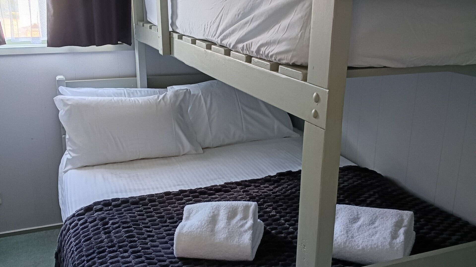 Un lit superposé avec une literie blanche et une couverture tissée de couleur foncée.