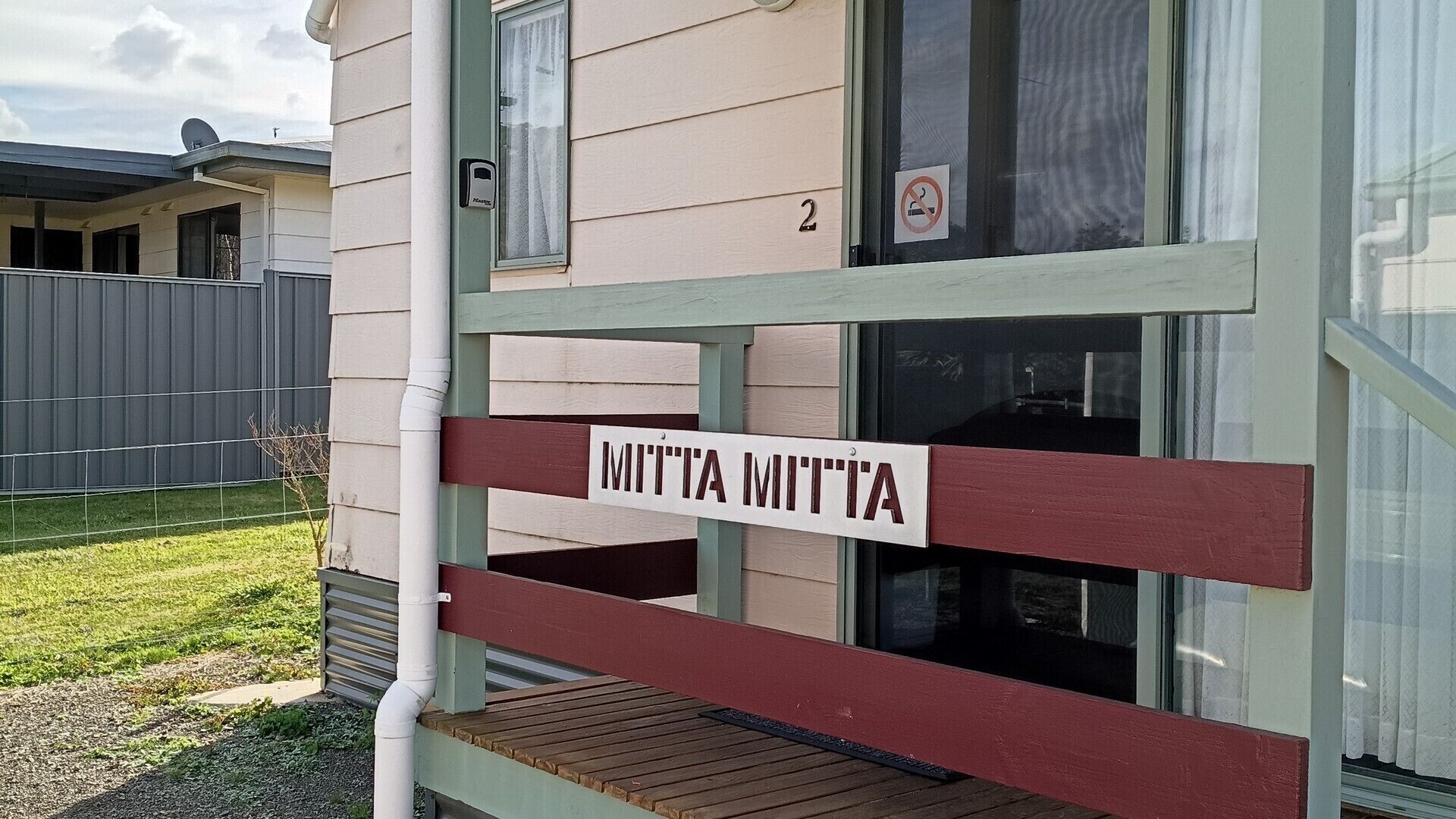 A wooden deck with a sign reading 'MITTA MITTA' and a house number '2' above a window.