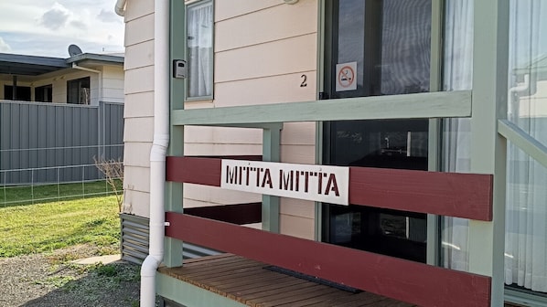 A wooden deck with a sign reading 'MITTA MITTA' and a house number '2' above a window.