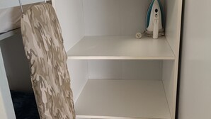 A corner of a room with a camouflage-patterned item hanging on the wall, a white shelf with a small object on it, and a white wall.