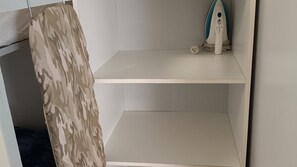 A corner of a room with a camouflage-patterned item hanging on the wall, a white shelf with a small object on it, and a white wall.