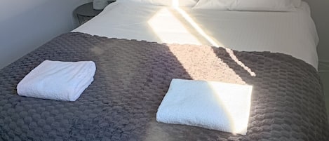 A bed with a textured blanket and two folded white towels.