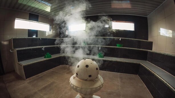 A room with a central decorative object emitting steam, surrounded by dark tiled walls and a tiled floor.