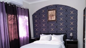 A hotel room with a bed, a nightstand, a lamp, and a wall with a decorative pattern.