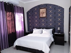A hotel room with a bed, a nightstand, a lamp, and a wall with a decorative pattern.