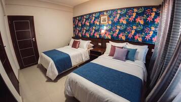 Habitación de hotel con dos camas, cabecera estampada con motivos florales, una puerta y una ventana con cortinas.