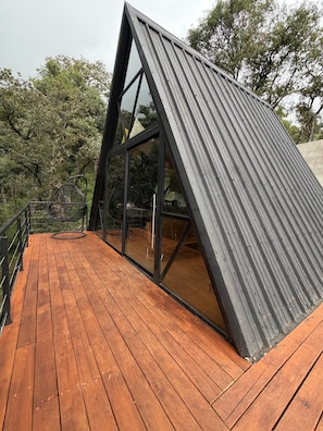 A modern, triangular metal structure with a wooden deck and glass windows.
