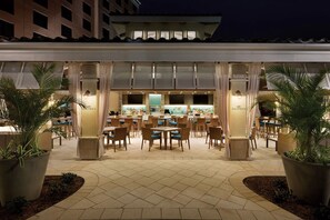 An outdoor restaurant area with tables and chairs, a bar in the background, and potted plants. - Queen Suite at Caribe Royale Orlando - Sports Court & Resort Fun Included! (Orlando)