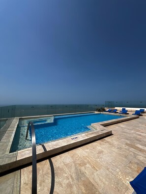 Ein Pool auf dem Dach mit klarem, blauem Wasser, umgeben von einer Steindeck und blauen Liegestühlen.