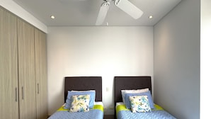 Quarto com duas camas de solteiro, um ventilador de teto e um guarda-roupa.